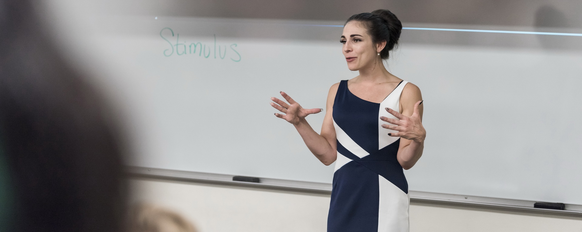 A psychology professor gestures while talking in front of a whiteboard